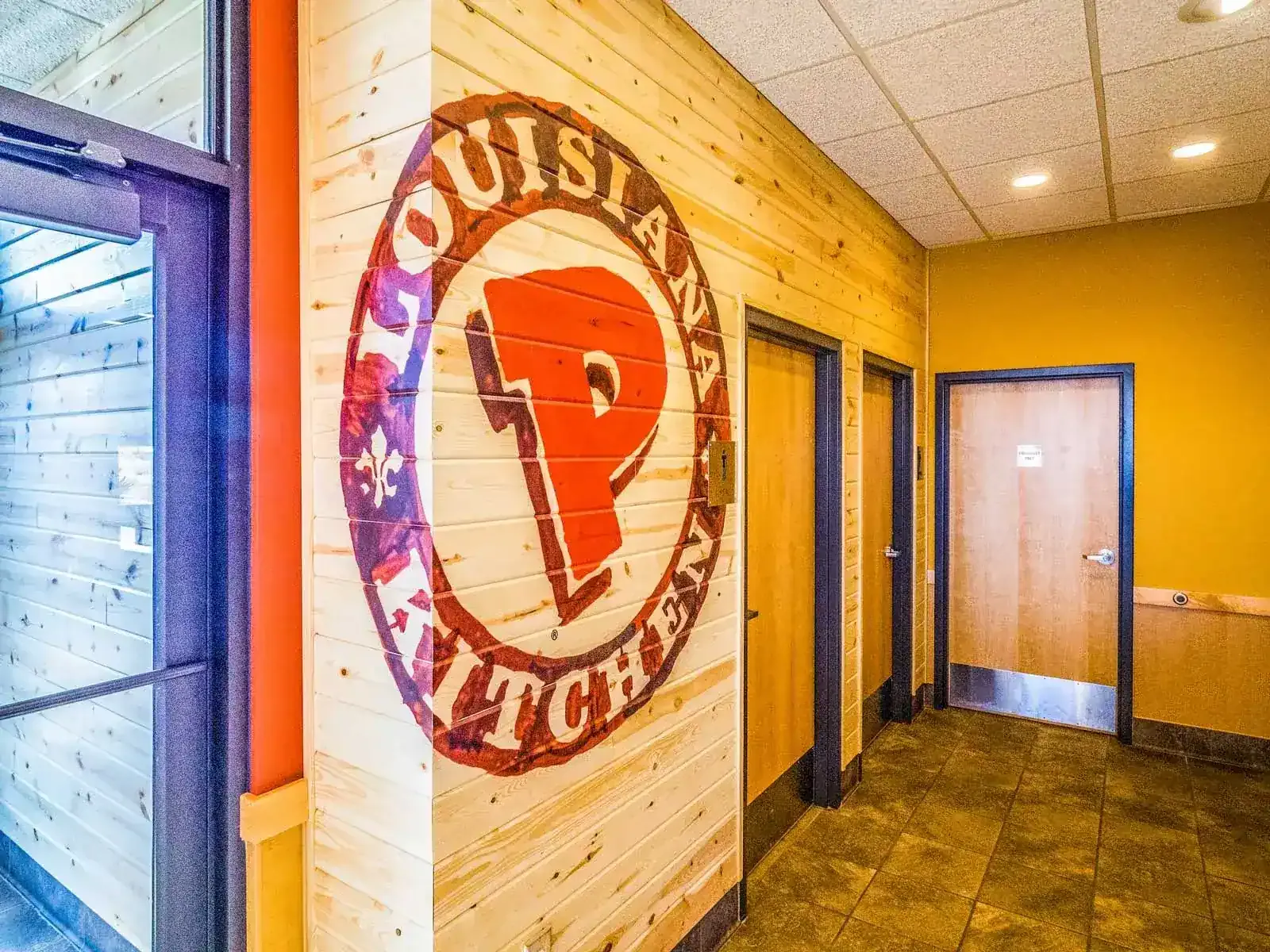 Painted Louisiana Kitchen logo on a wood-plank wall beside the restroom doors.