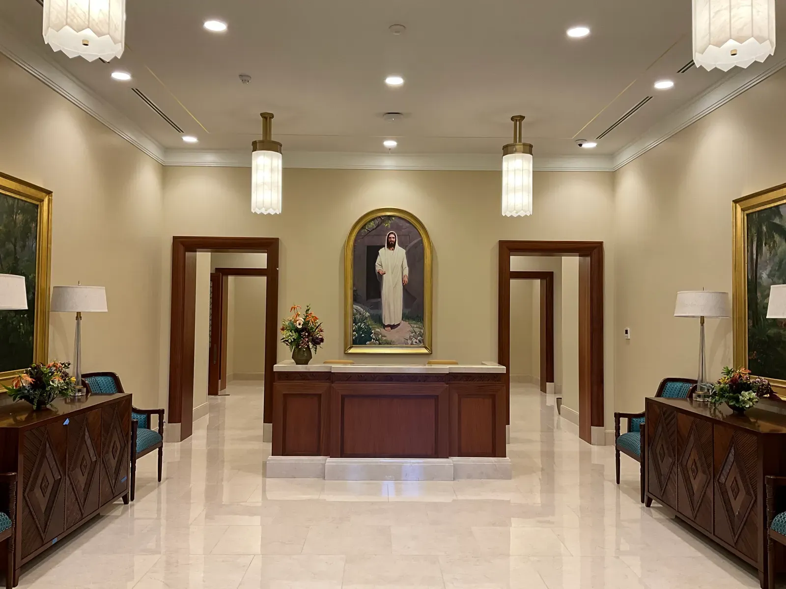 Reception desk beneath a framed painting, with wood doorways, carved side cabinets and a white stone floor.