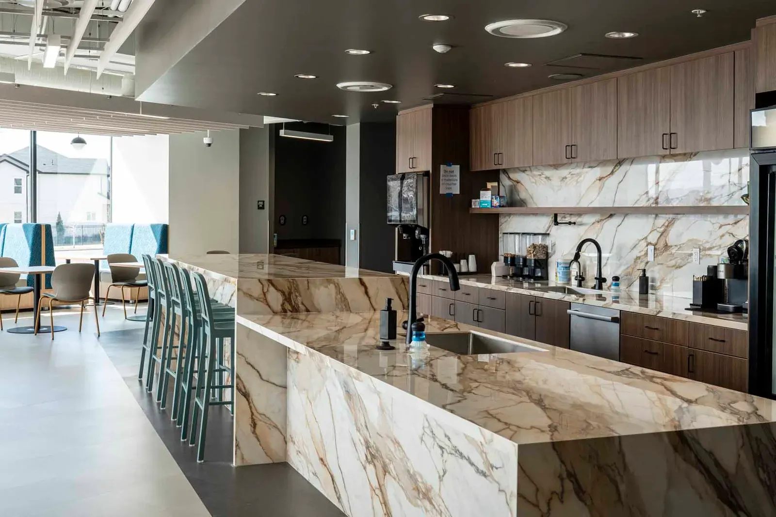 Marble kitchen island with a sink and teal bar stools, with wood cabinets behind.