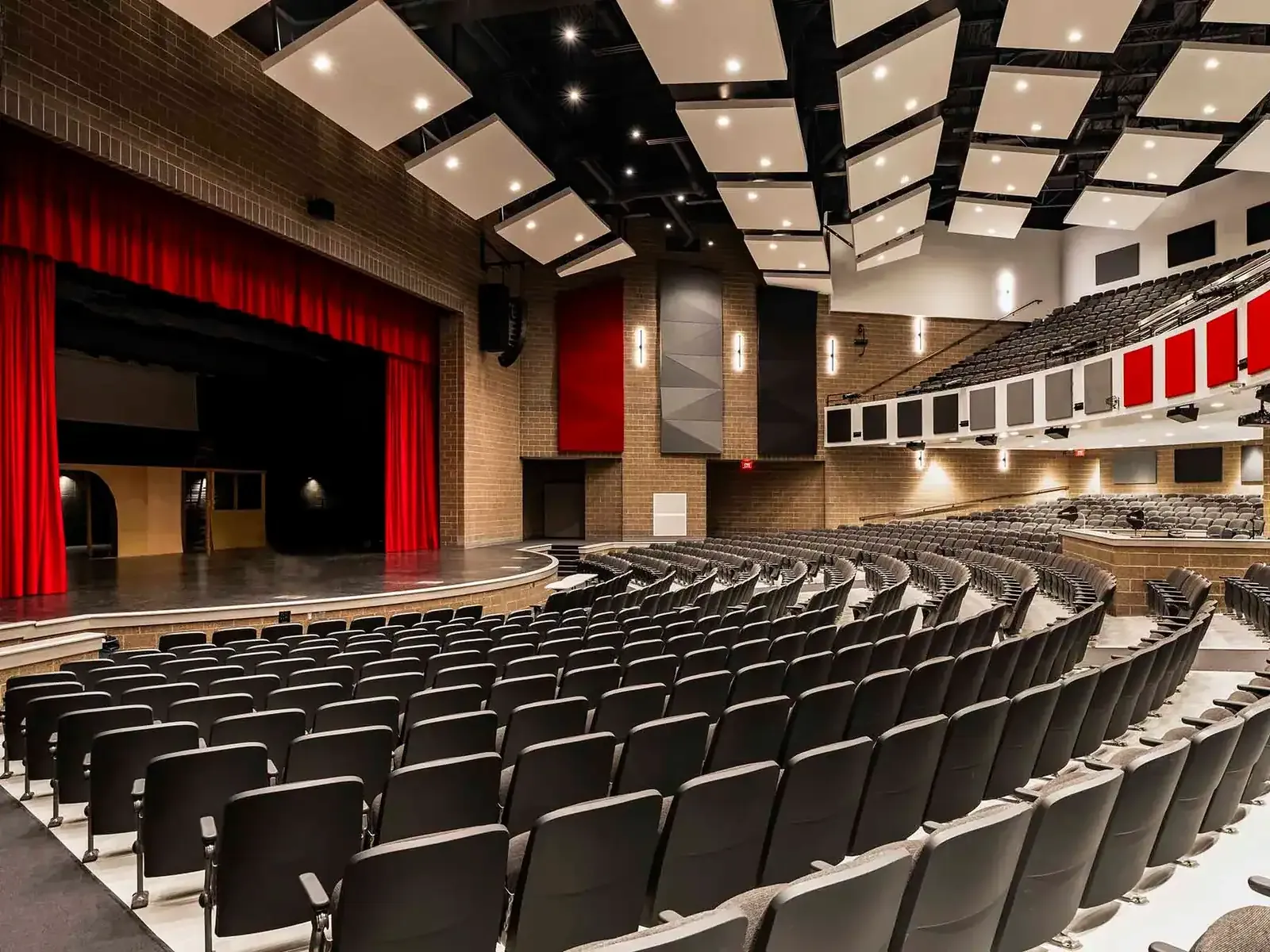 Auditorium with red stage curtains, tiered seating, and white ceiling panels.