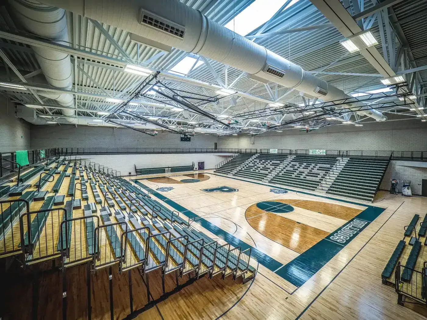 Main gymnasium with a wood floor, retractable bleachers on both sides and an exposed steel roof structure