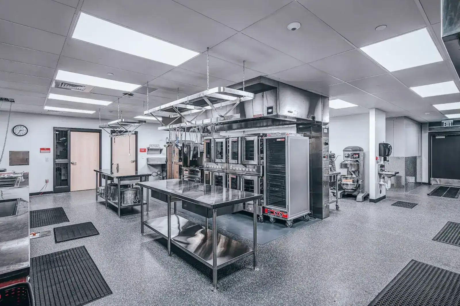 Commercial kitchen with stainless steel prep tables, convection ovens and a mixer