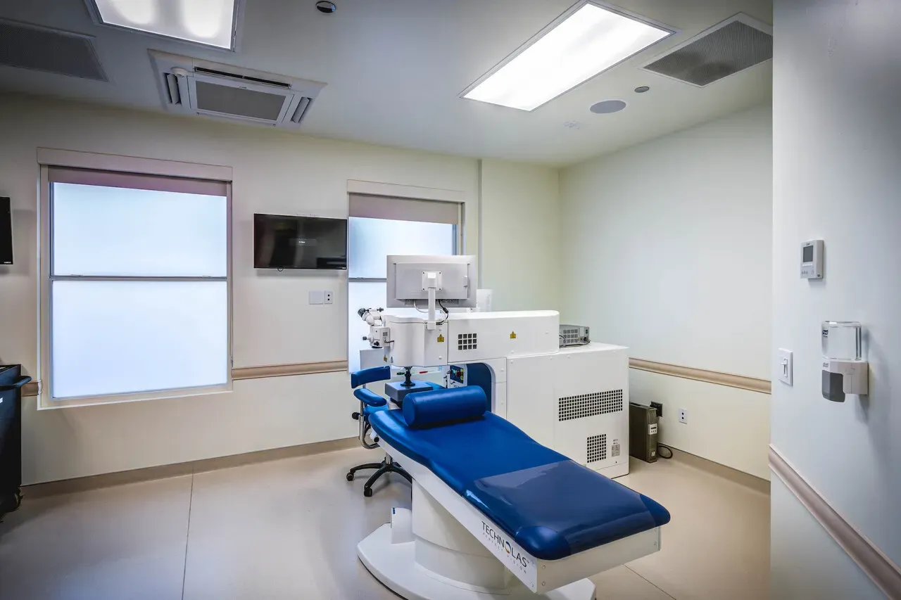 Laser procedure room with a blue patient chair, an equipment console, and two windows.