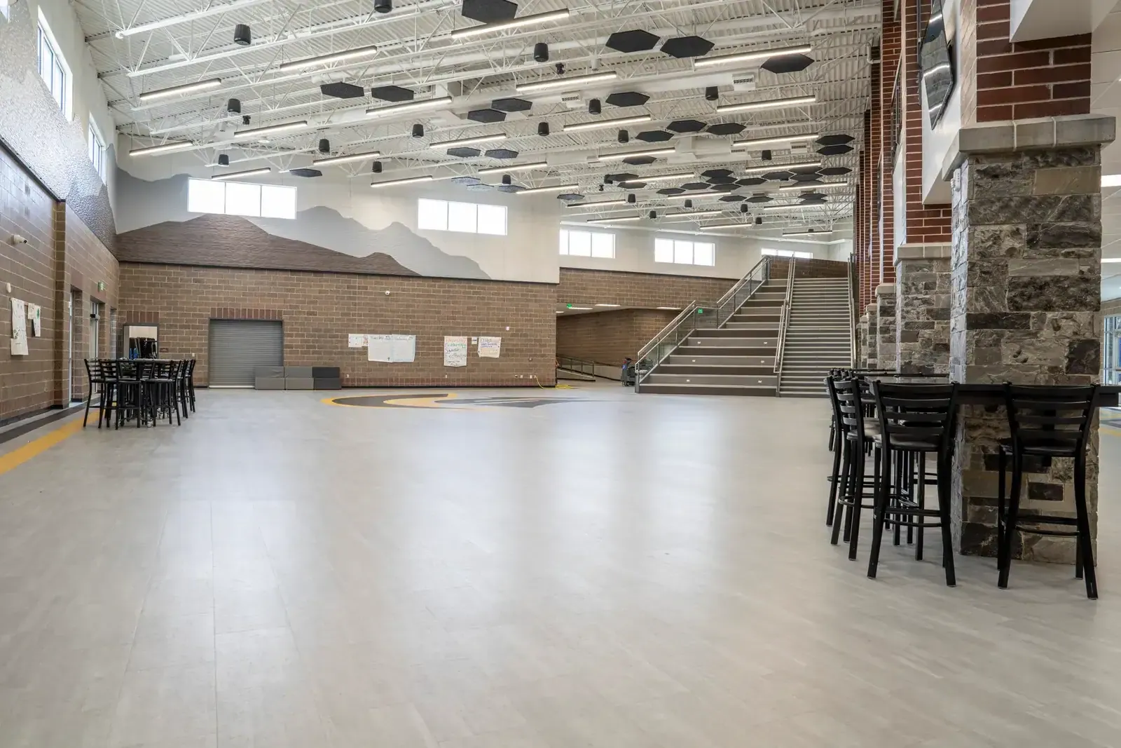 Wide commons with gray flooring, a wide staircase, stone-clad columns and black bar-height tables.