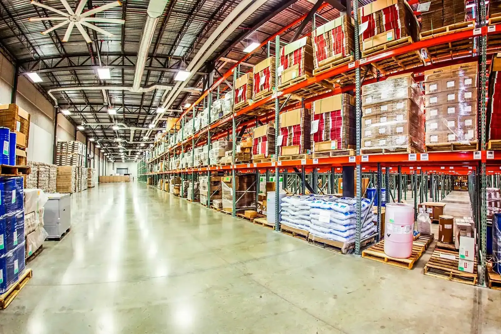 Warehouse aisle with orange pallet racking stocked with boxes and wrapped pallets.