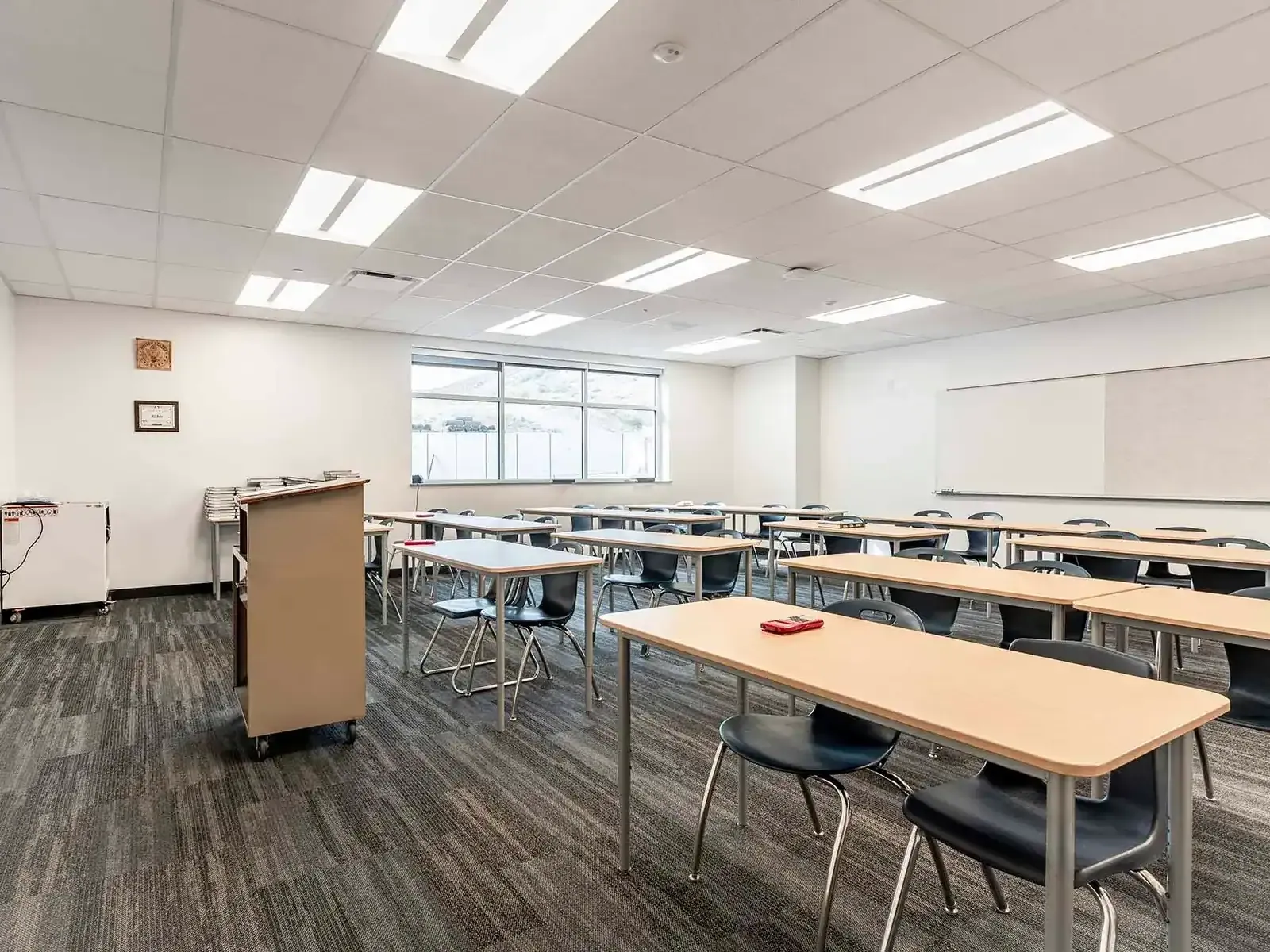 Classroom with long tables, black chairs, a mobile lectern, and a whiteboard