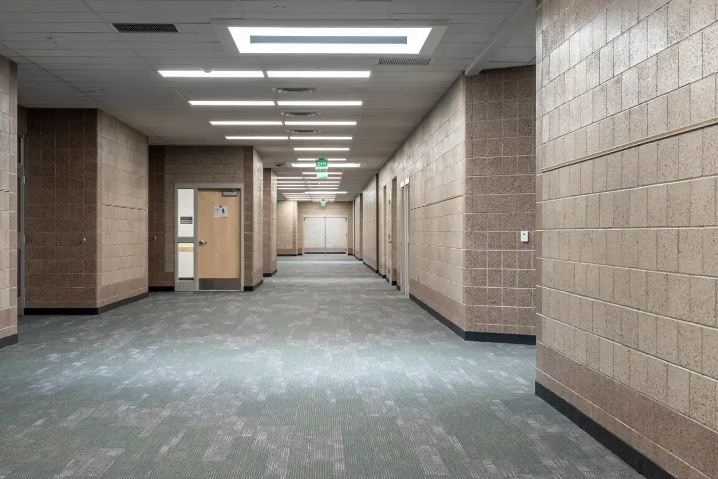 Corridor with tan block walls, patterned green-gray carpet and a wood door on the left.
