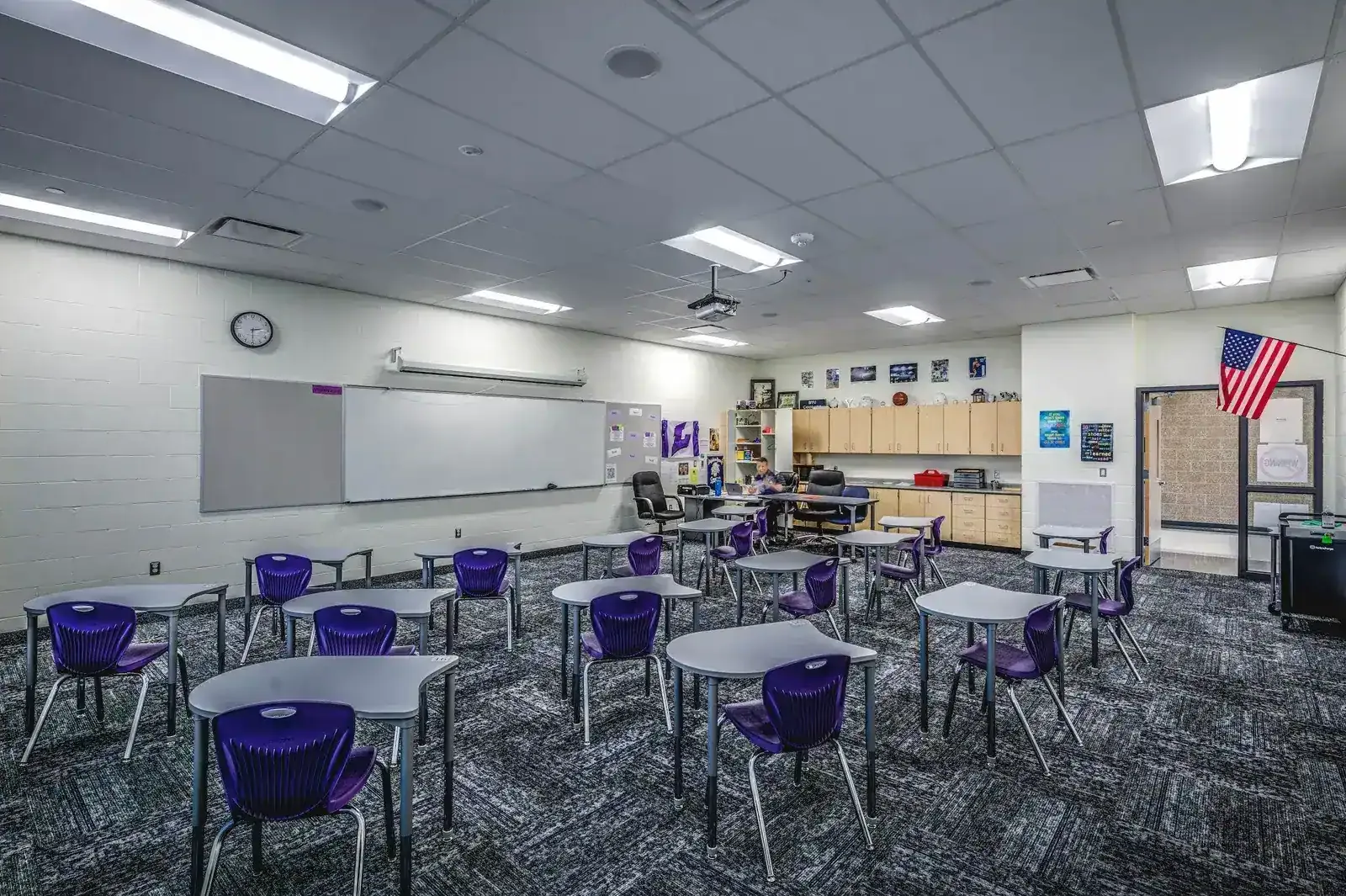 Classroom with purple student chairs, desks, whiteboards and wood cabinets.