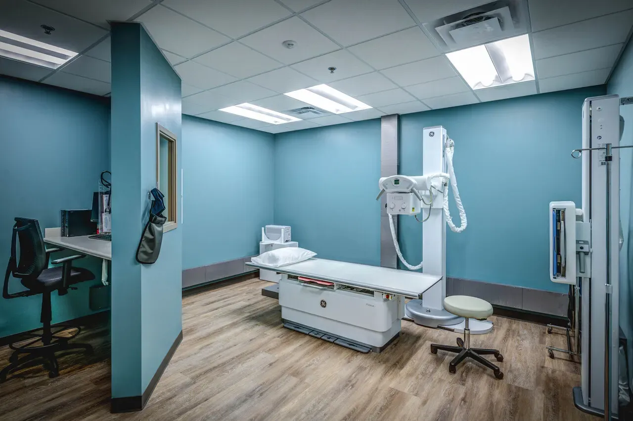 X-ray room with a radiography table and overhead tube.