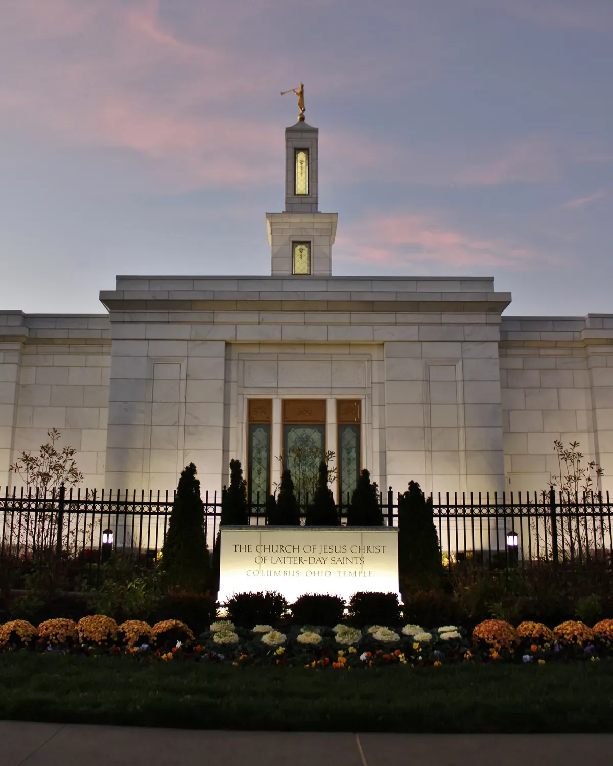 Close view of the stone spire with a gold figure blowing a trumpet on top and narrow art glass windows below, against a dusky sky.