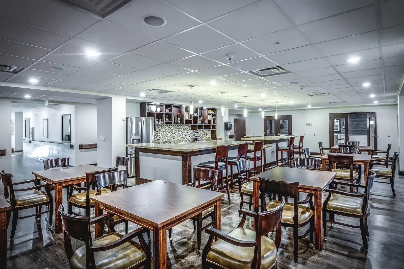 Dining area with wood tables and chairs and a serving counter in the background.