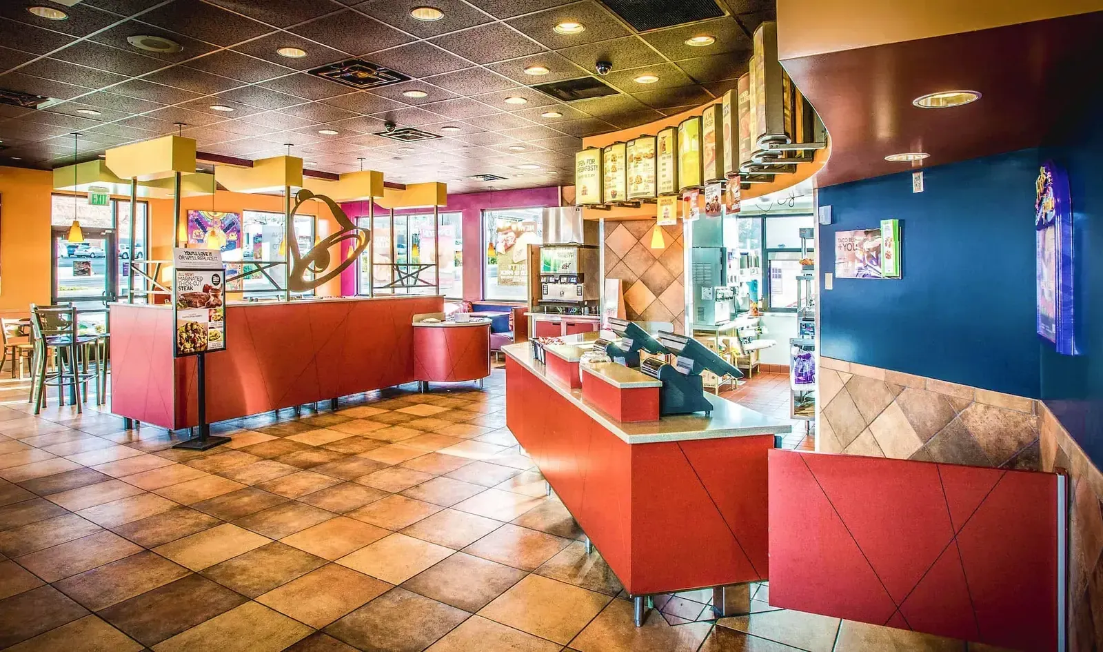 Ordering counter and dining area with red counters, a tile floor and an angled yellow ceiling soffit.