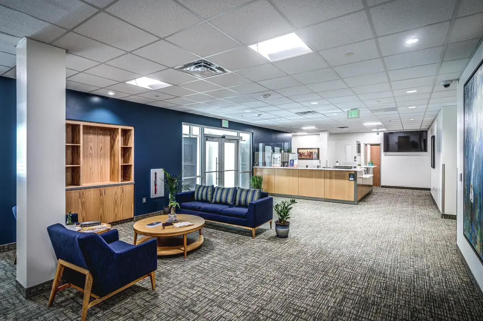 Lobby seating area with a blue sofa and chairs, and a front desk in the background