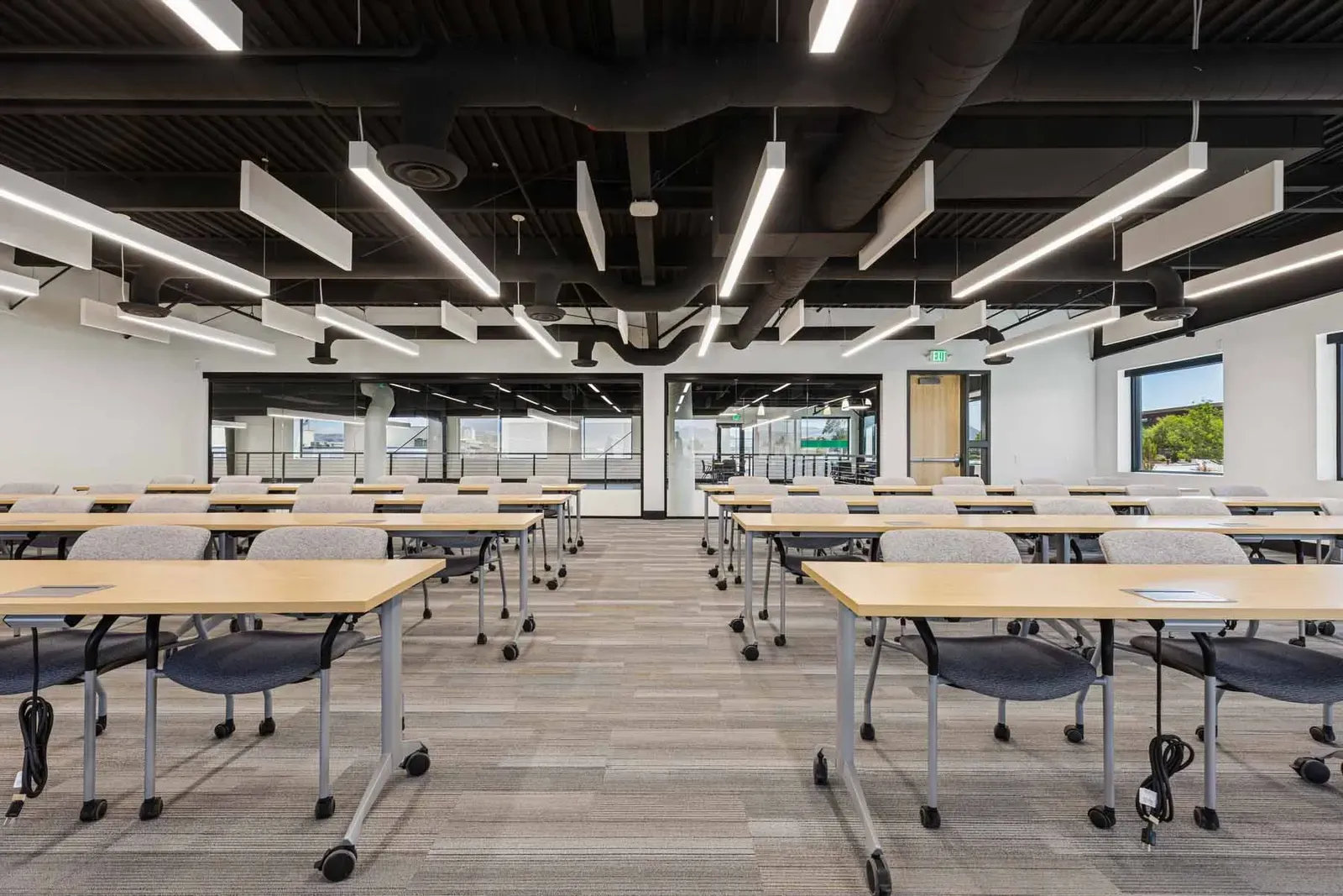 Training room with rows of tables and chairs under a black exposed ceiling with linear lights.