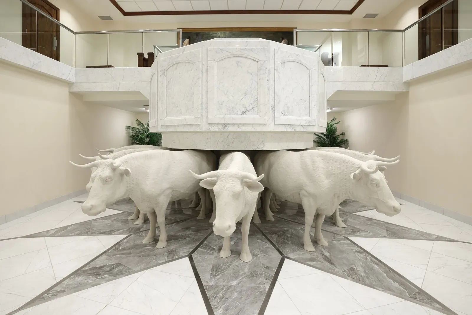 Baptismal font in a marble case resting on white carved oxen, with glass railings above and a star-patterned marble floor