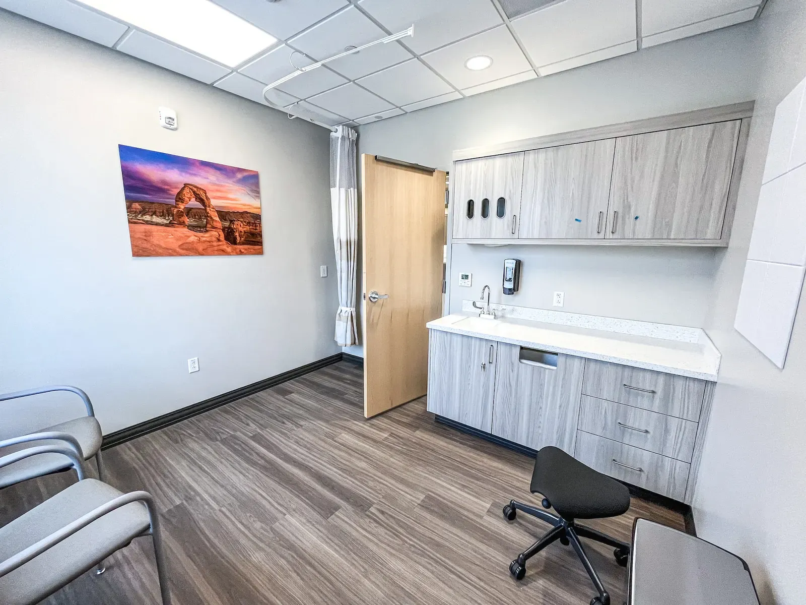 Exam room with a wood door, a sink and cabinet counter, and landscape artwork of a red rock arch