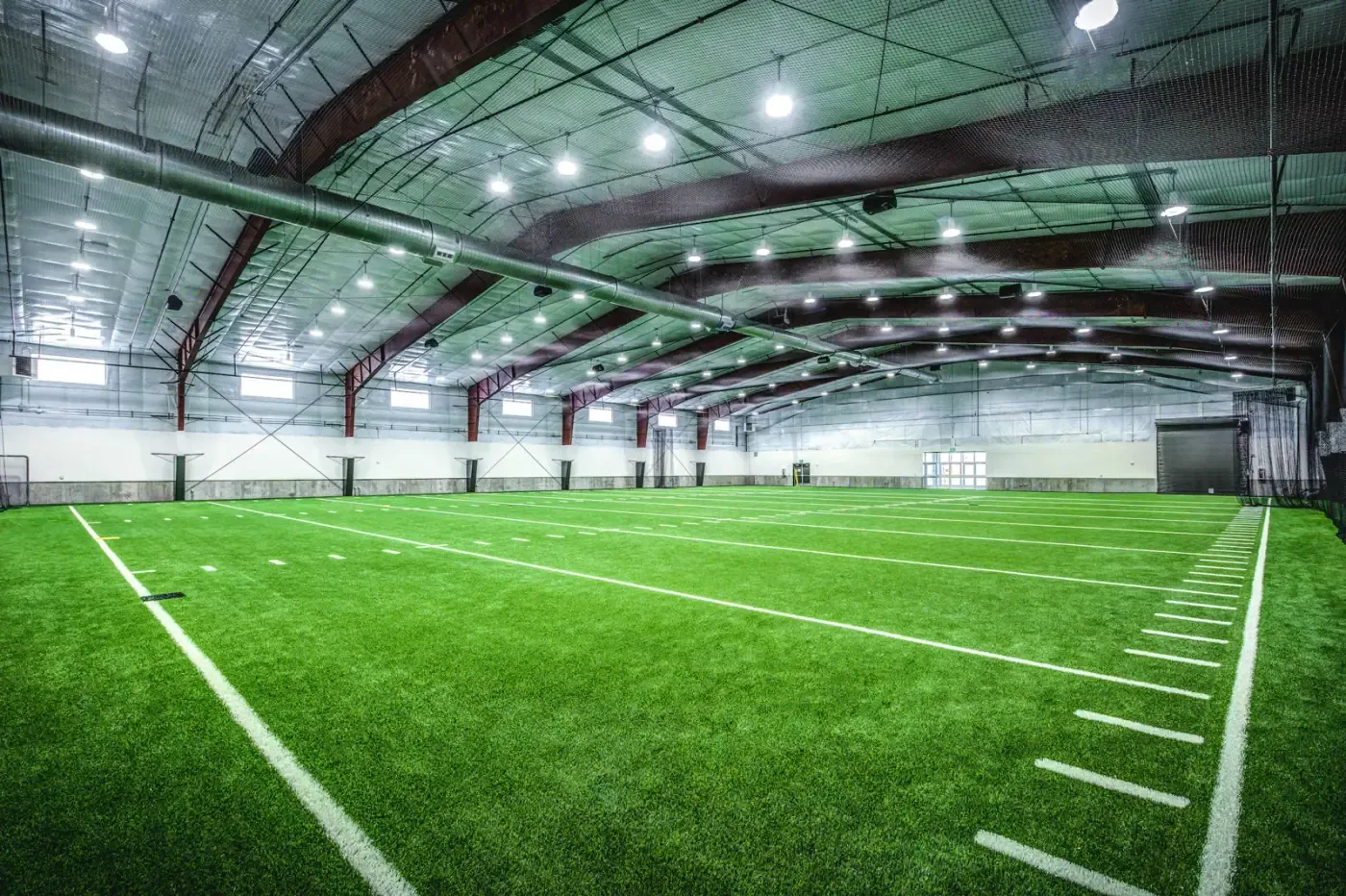 Inside the training facility, an artificial turf field under steel roof framing