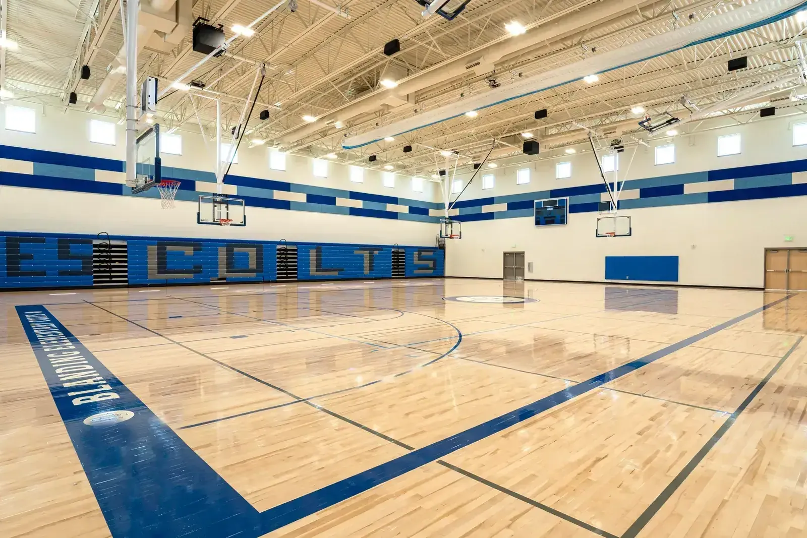 Gymnasium with a maple wood floor, blue and white walls lettered COLTS and basketball hoops overhead.