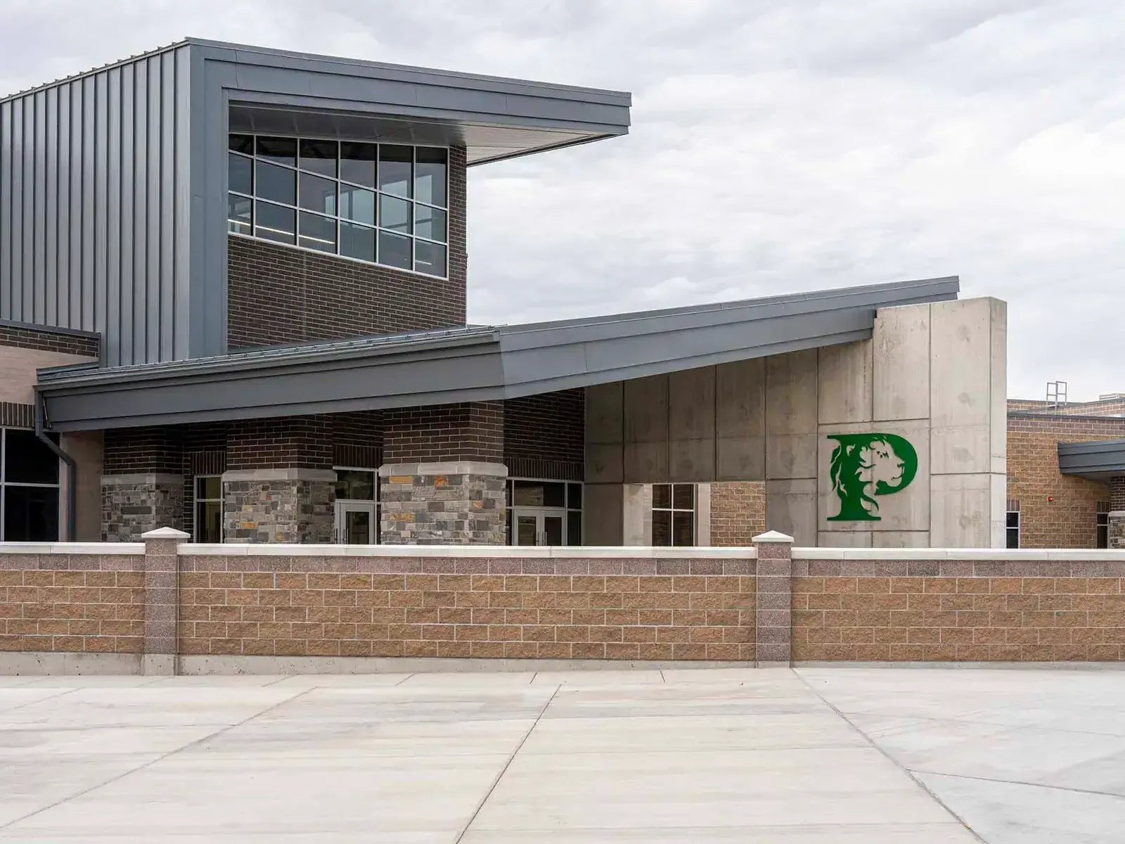 School entrance with an angled metal roof, brick and stone walls and a green lion P logo on a concrete panel