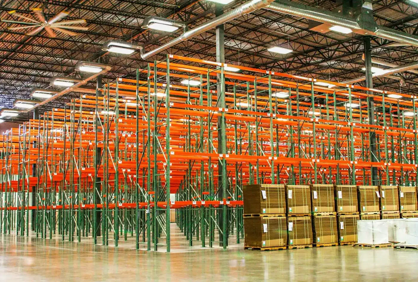 Rows of orange and green pallet racking under the steel roof.