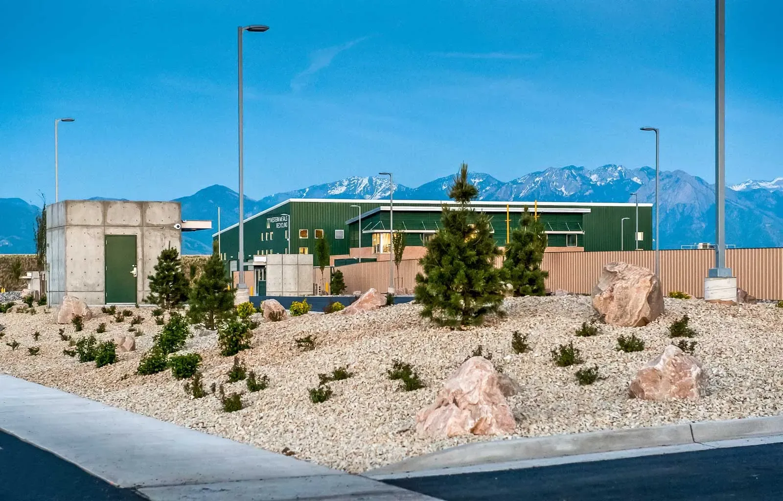Landscaped rock garden with boulders and small evergreens, the green building and mountains in the distance