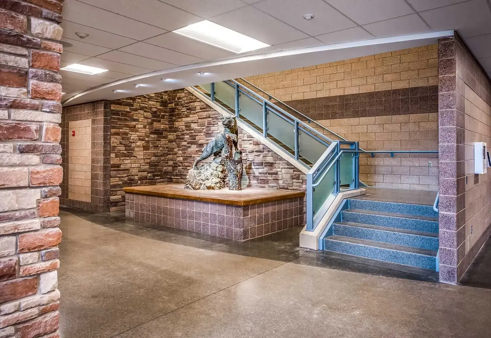 Stairway with a glass railing and a bronze animal sculpture on a stone-and-tile base