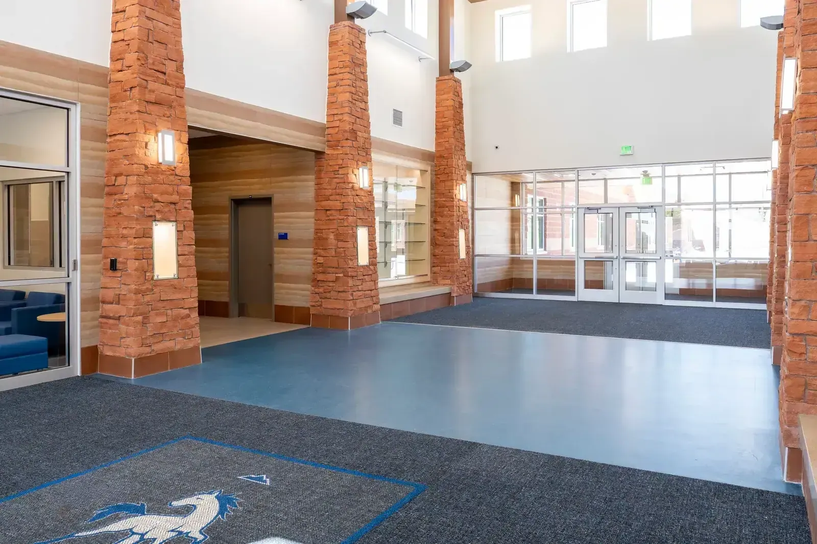 Entry lobby with tall red stone columns, a blue floor and glass doors under high windows.