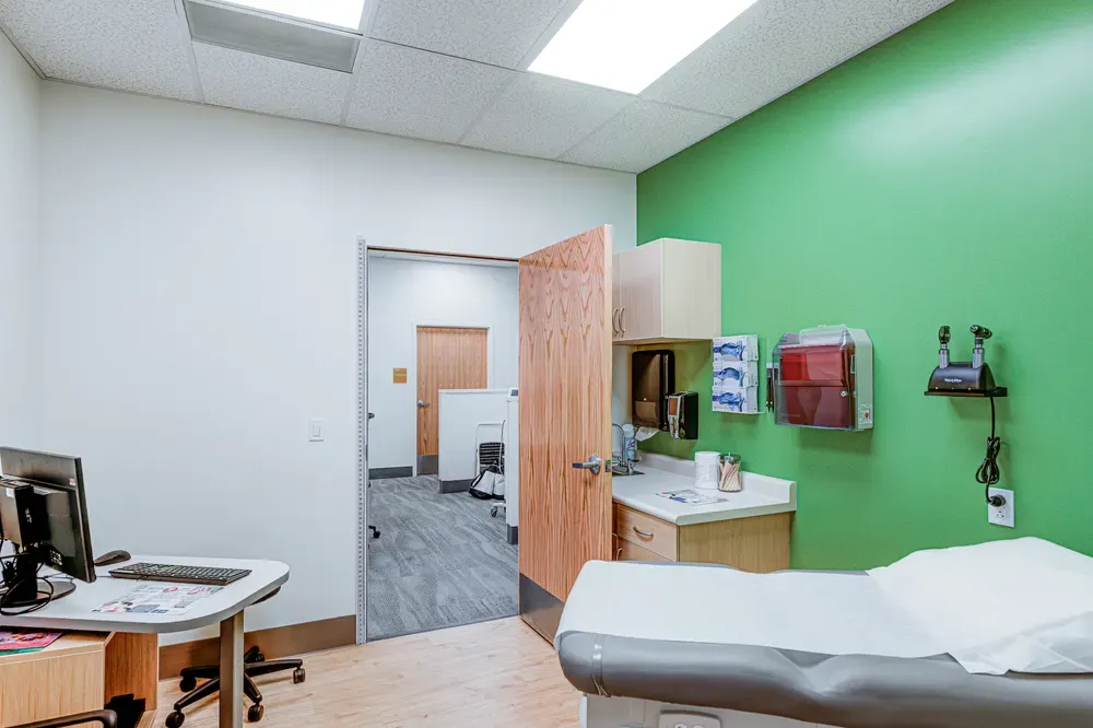 Exam room with a green accent wall, an exam table and a desk.