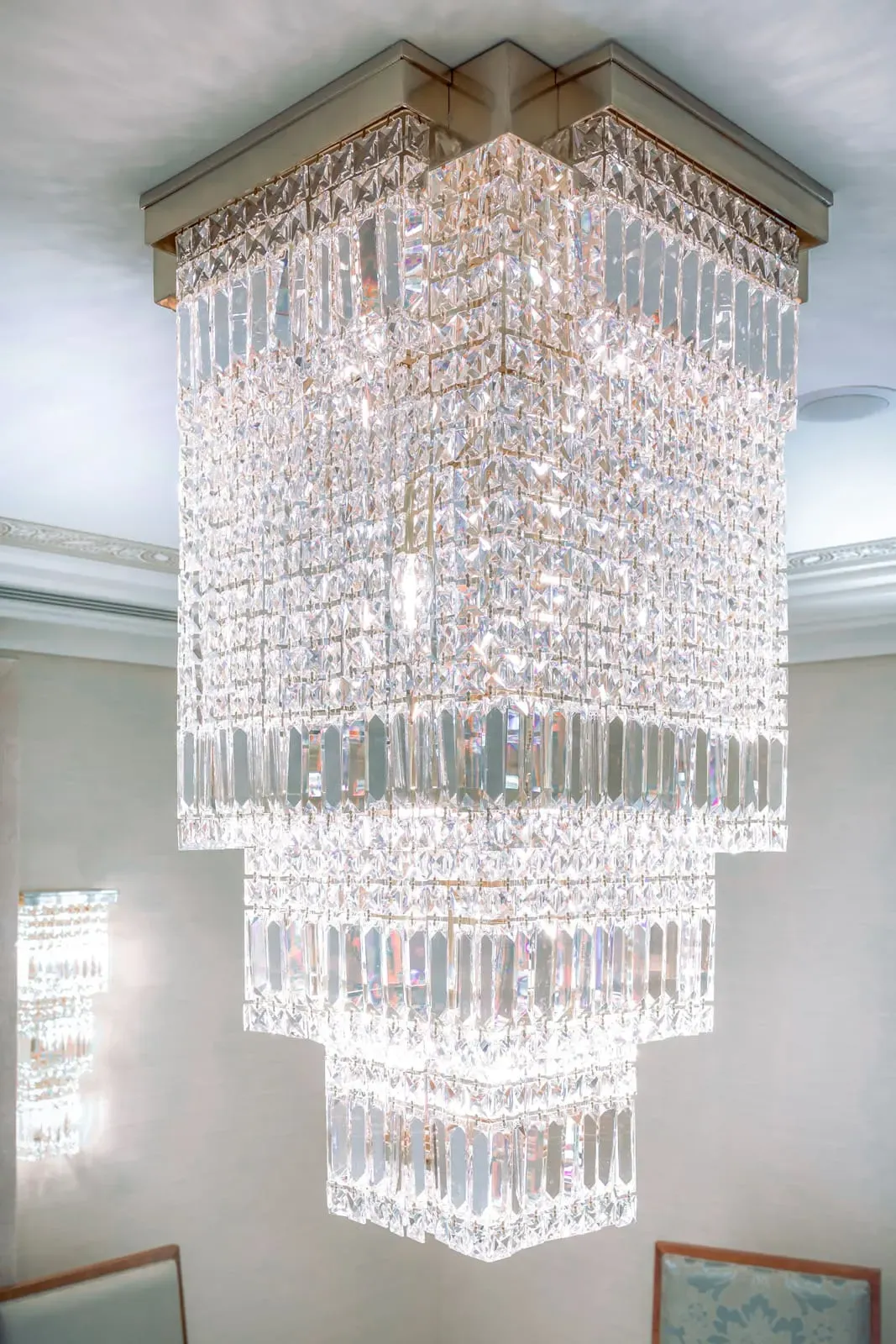 Close view of a tiered, square crystal chandelier hanging from a molded ceiling