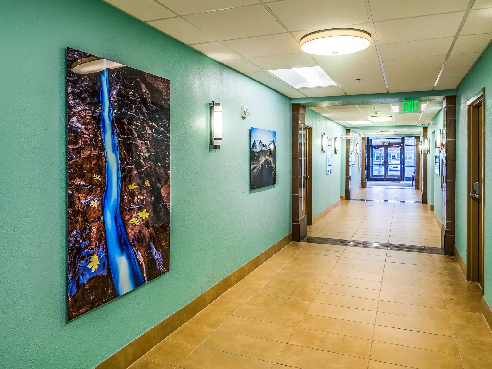 Corridor with tile floor and teal walls, with a large framed photograph of a waterfall canyon.