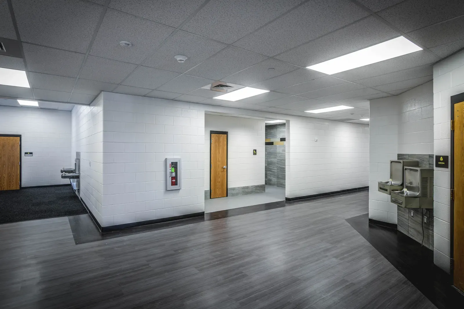 Interior corridor with drinking fountains, wood-toned doors and a gray plank-look floor