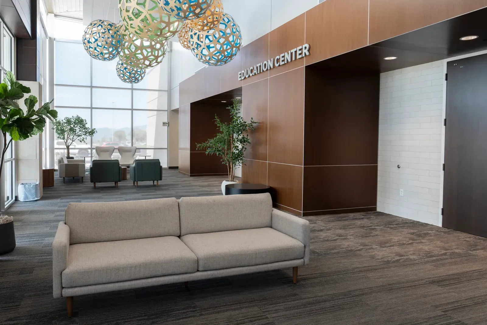 Education Center entrance with a wood-paneled wall, a sofa and woven pendant lights beside a window wall.