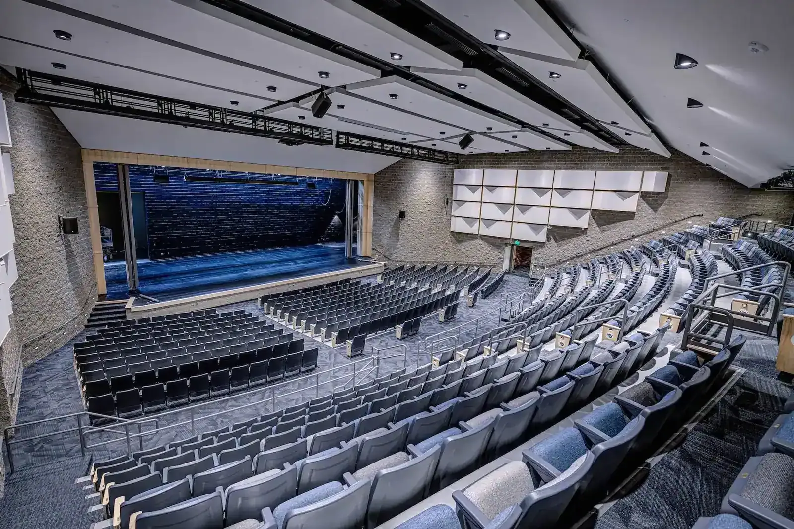Auditorium seen from the back, with tiered blue seating and a stage.