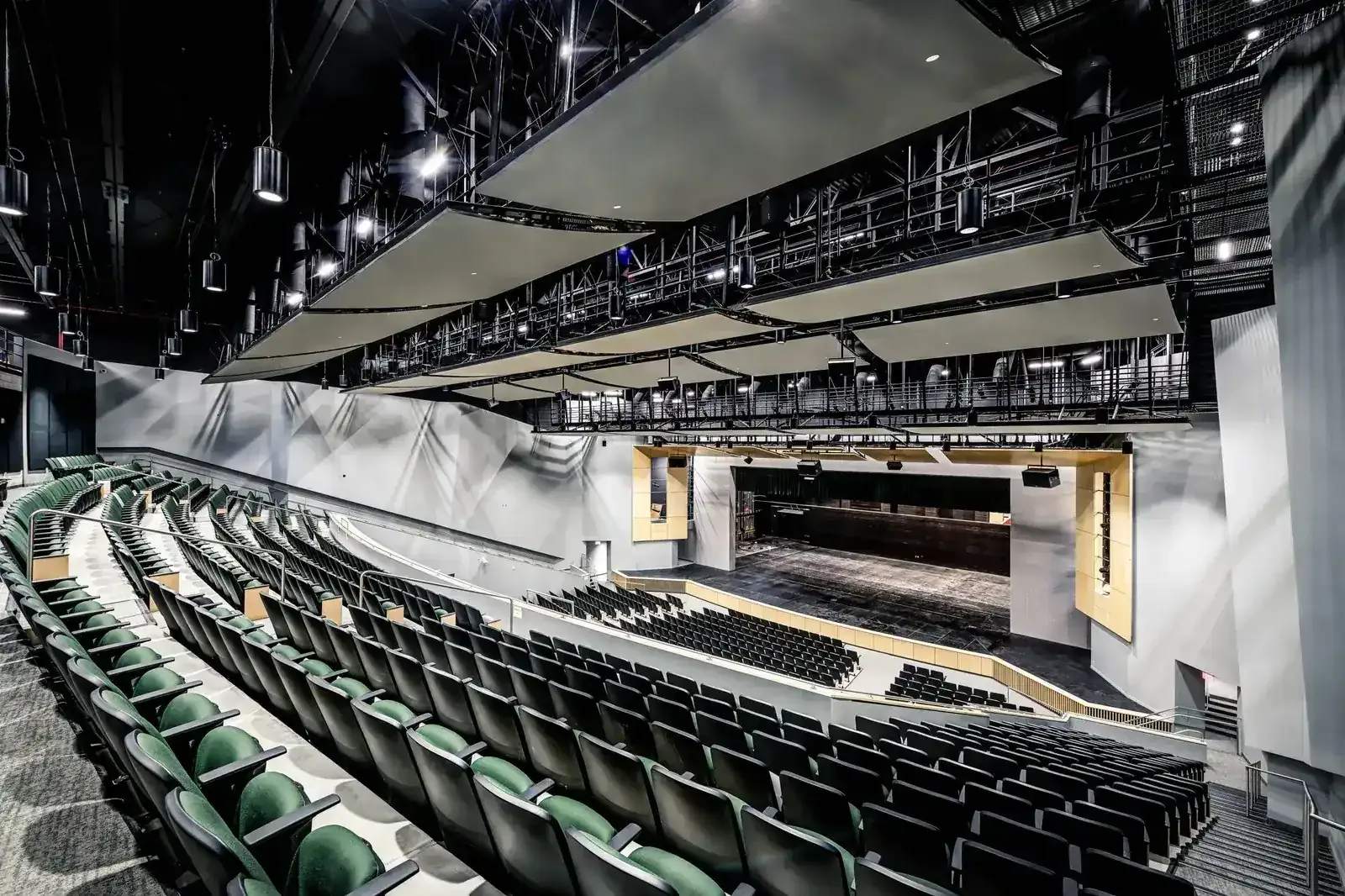 Performing arts auditorium with green seats sloping toward a wide stage and a lighting grid overhead