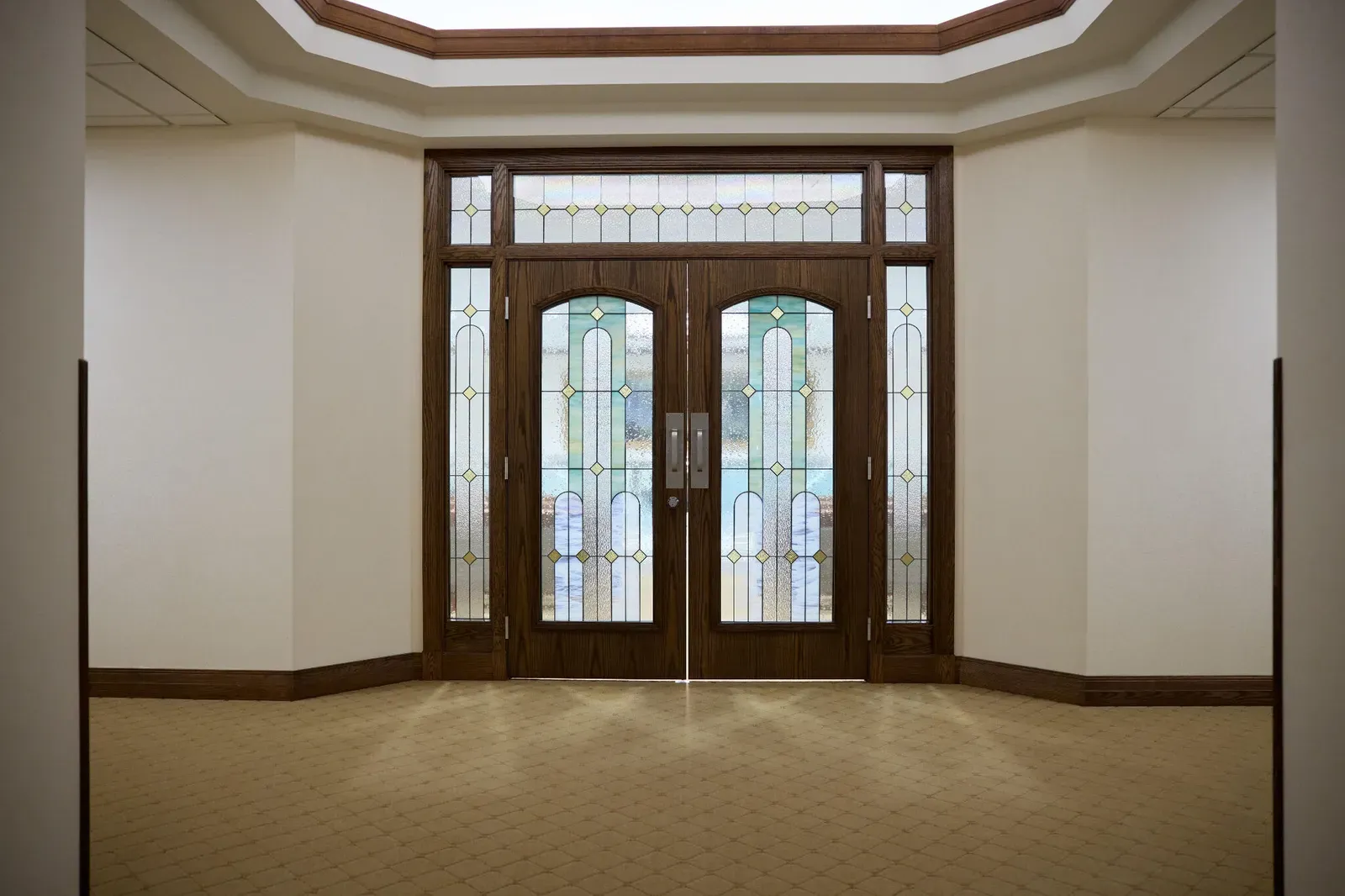 Pair of wood doors with stained-glass panels and side lights in a room with a skylight recess and a tile floor