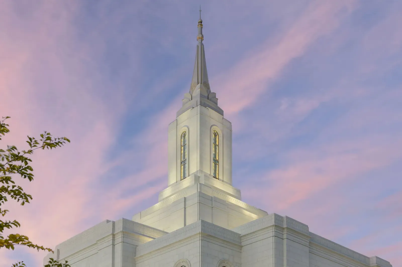 Close view of the temple spire and upper tower, lit against a pink sky.