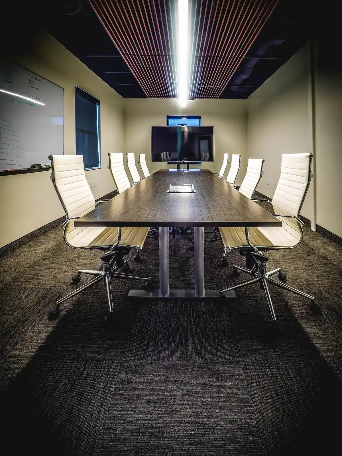 Conference room with a long table, white leather chairs, a wall-mounted screen, and a slatted wood ceiling
