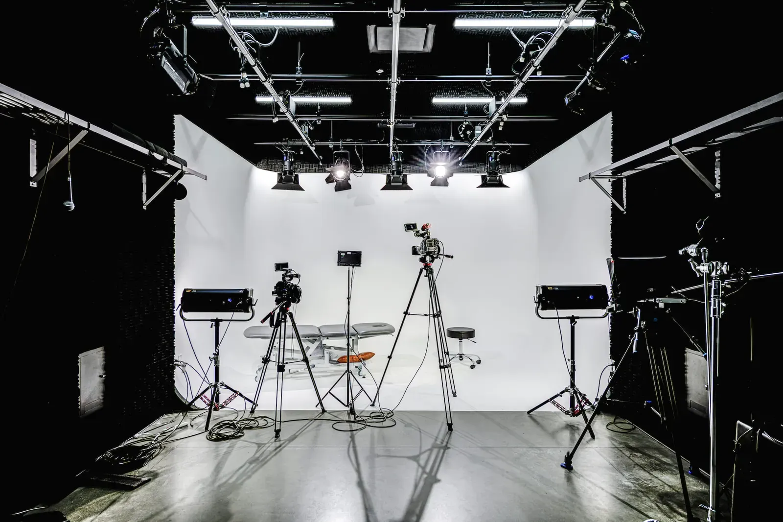 Production studio with a white backdrop, studio lights and video cameras on tripods.
