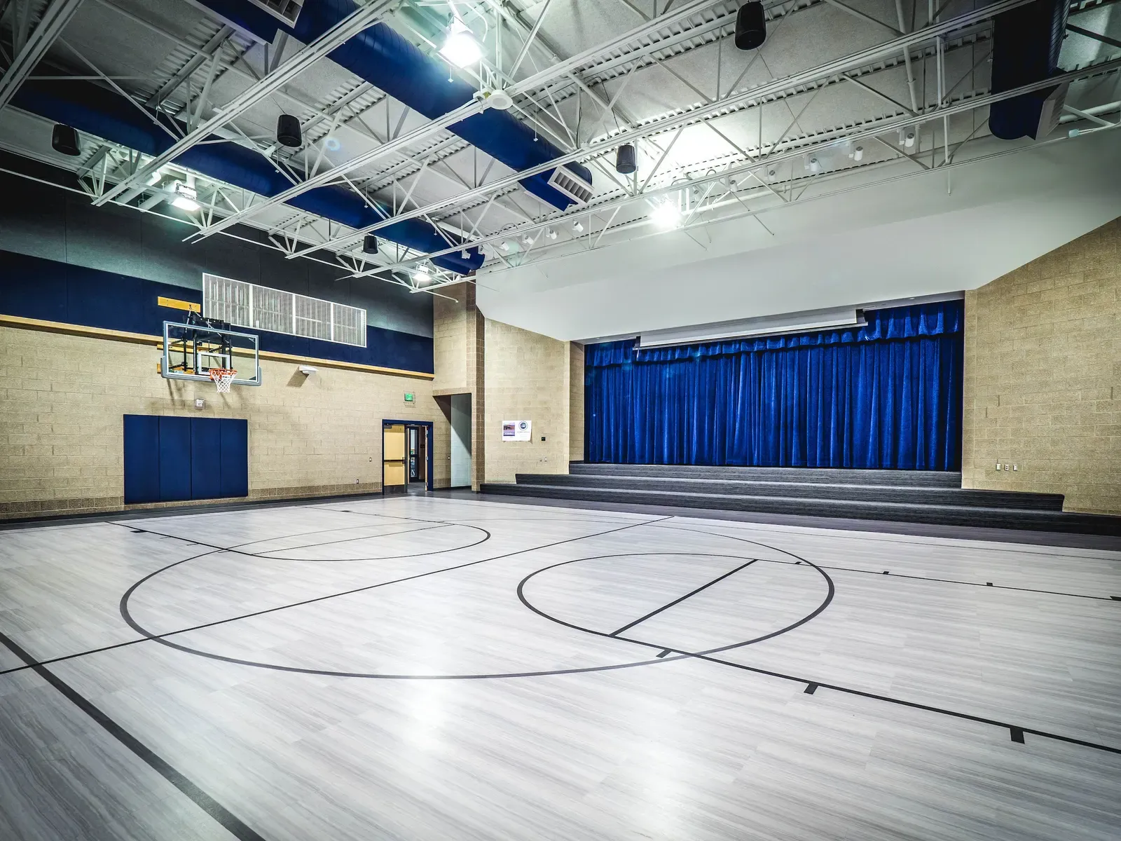 Multipurpose room with a basketball court, a stage, and blue curtains