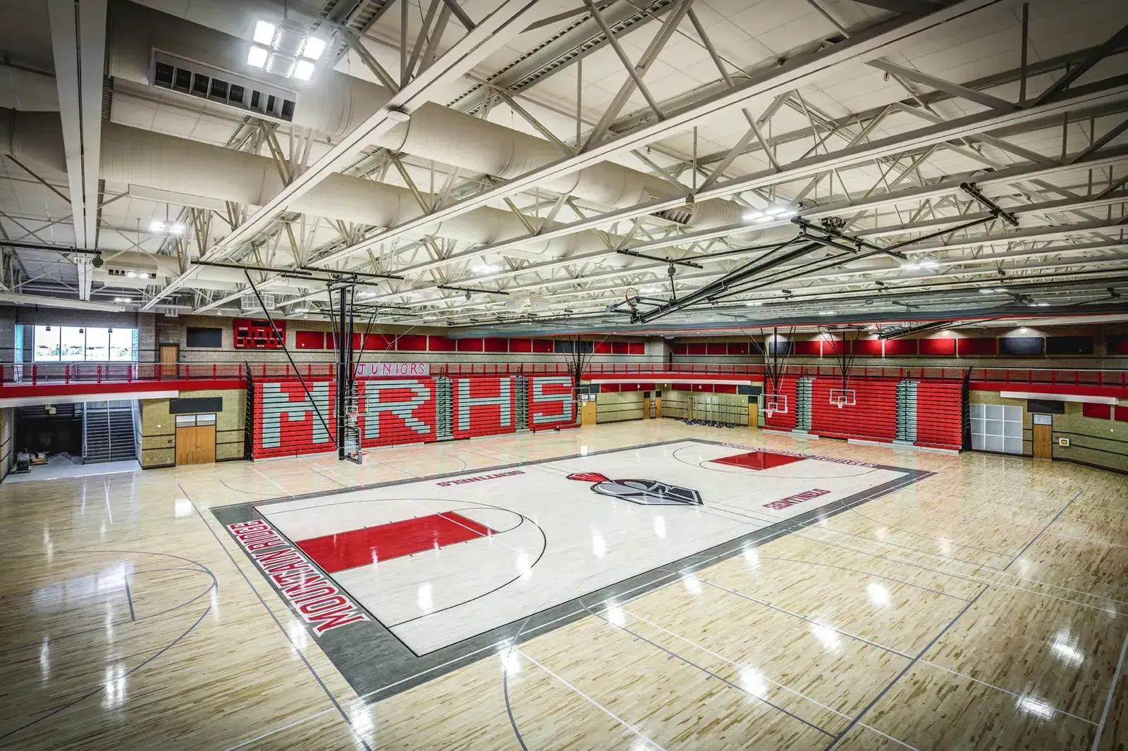 Gymnasium with a wood floor, red bleachers and the school initials on the wall.
