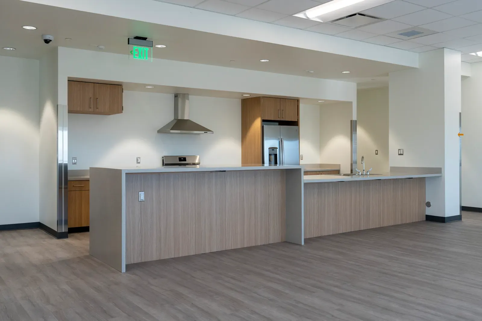 Open kitchen with a long island, wood cabinets, a range with a hood and a stainless refrigerator.