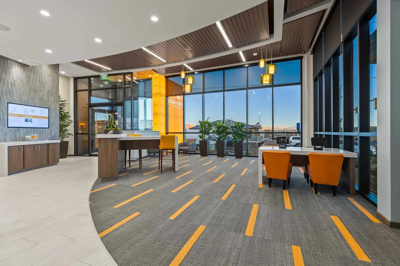 Branch lobby with a curved wood-slat ceiling, a glass curtain wall, orange chairs and carpet with yellow stripes.