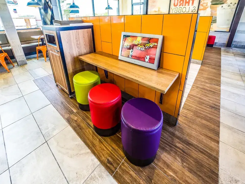 Counter-height ledge with colorful round stools and a wall-mounted screen against an orange panel wall.
