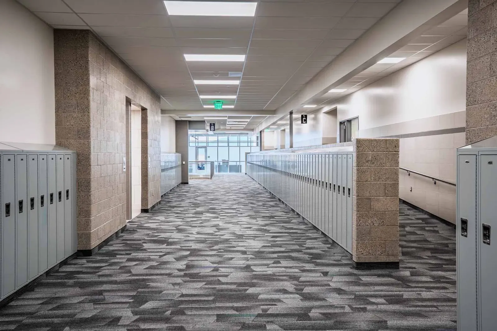 Corridor lined with lockers and tan block walls under linear ceiling lights.