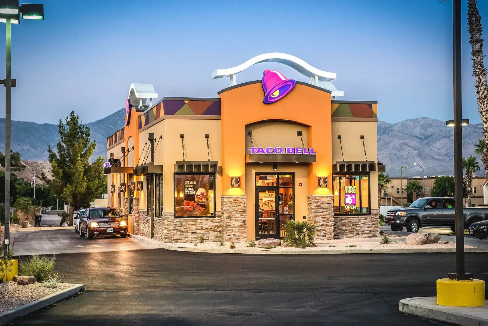 Corner view of the Taco Bell building at dusk with the bell logo above the entry and mountains behind