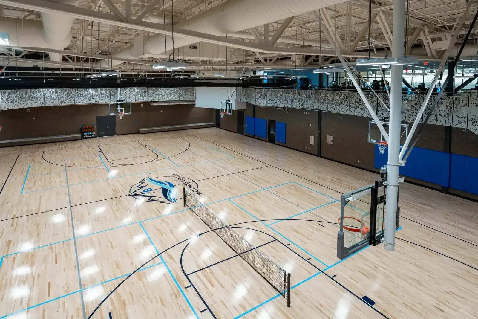Multi-use court seen from above, with a wood floor, a net, basketball hoops and a Wellness Center logo at center court.