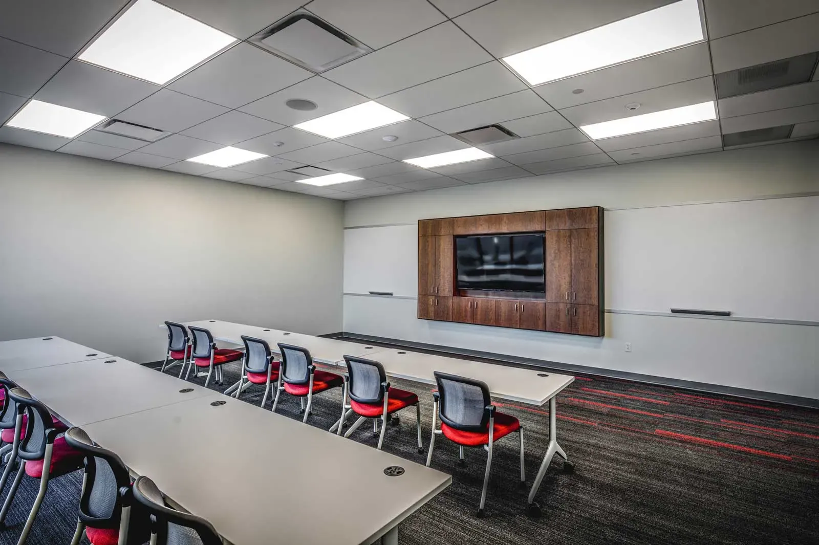 Training room with long tables, red and black chairs, whiteboards and a wall-mounted TV.
