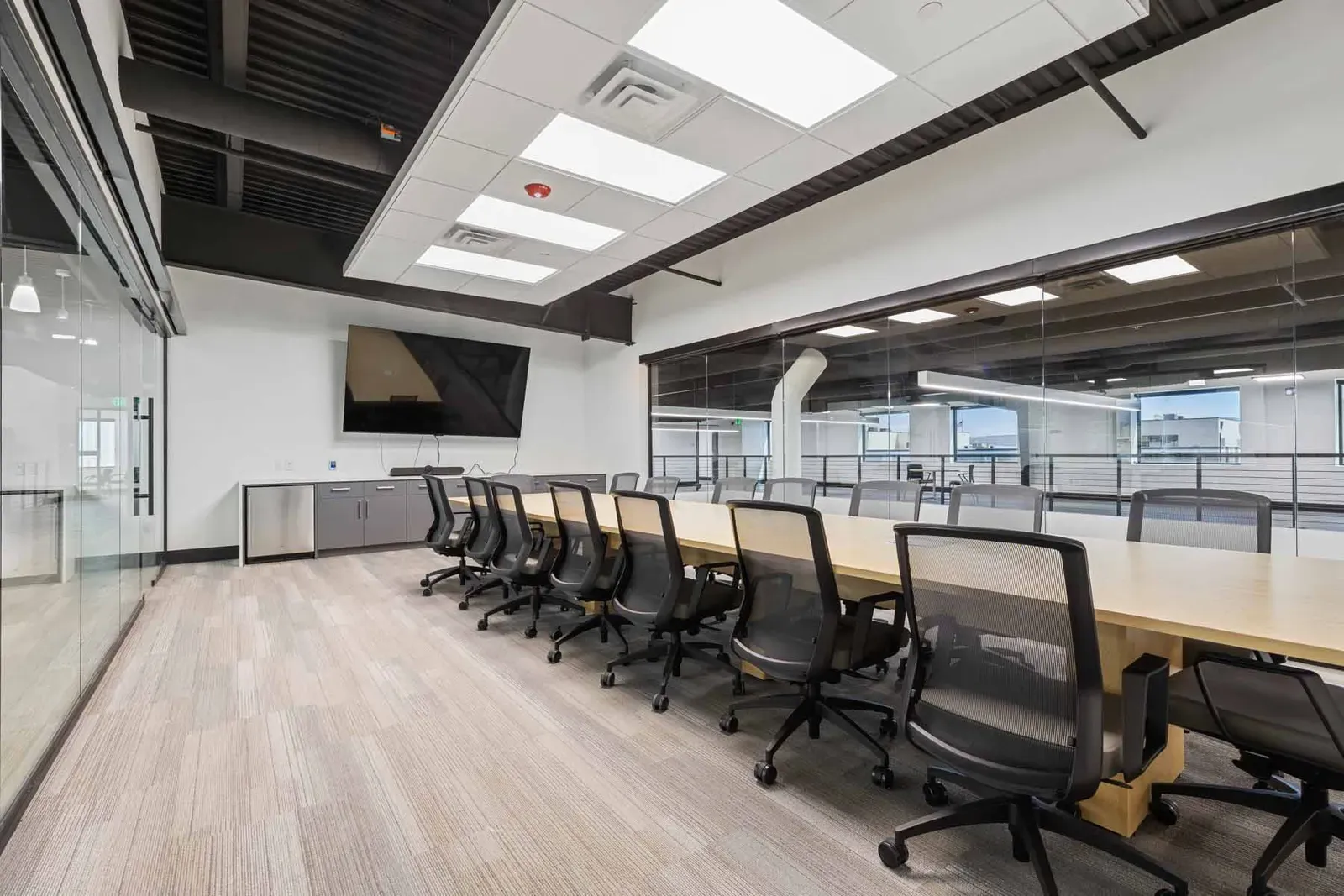 Conference room with a long wood table, a wall-mounted TV and glass walls.
