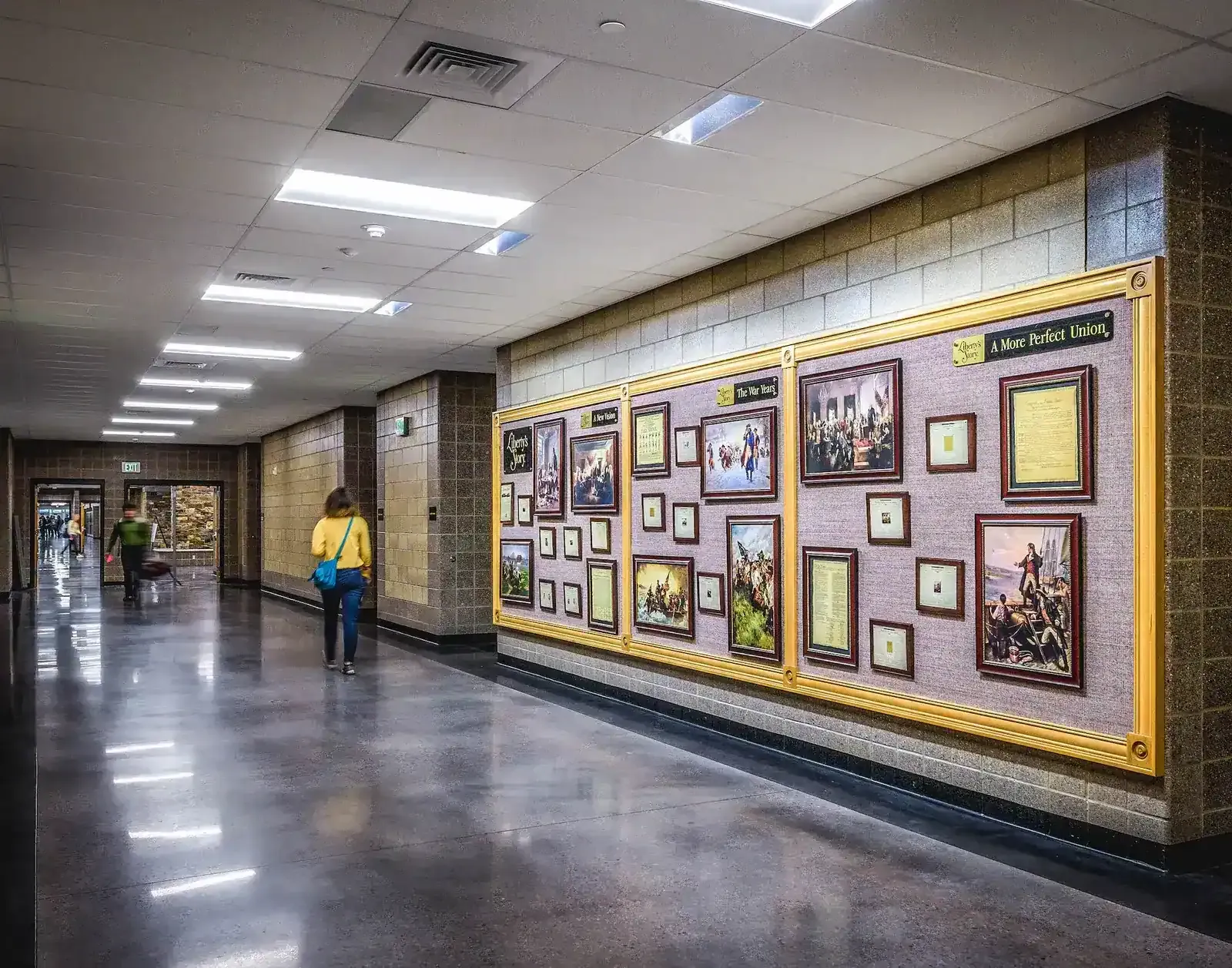 Hallway with a polished floor and a wall display of framed historical pictures and documents.