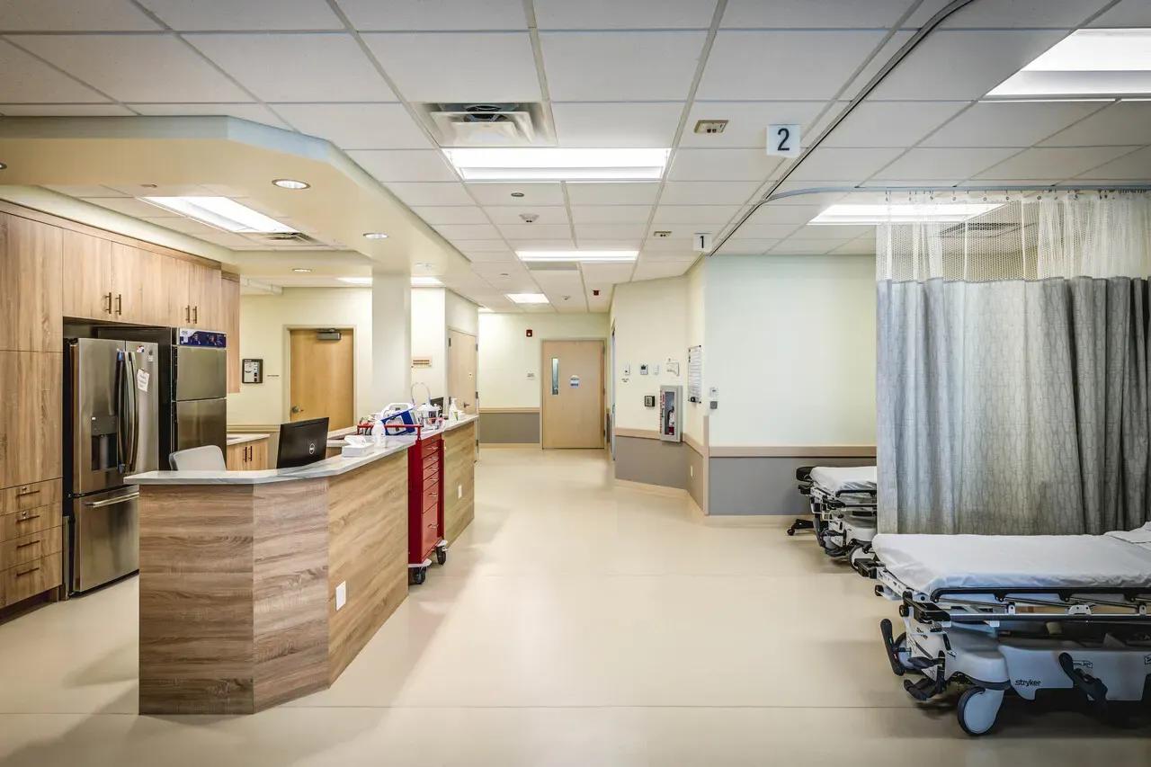 Corridor with a curved wood-look nurses' station and a curtained bay with a stretcher.